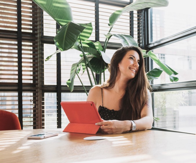 Smiling young woman in office with red tablet in front of big green flower