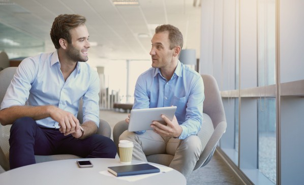 Two consulting men in office with blue shirts and tablet